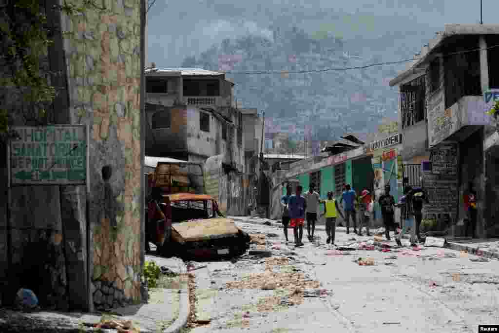 People walk past a damaged car in the Carrefour Feuilles neighborhood, which was deserted due to gang violence, in Port-au-Prince, Haiti, March 19, 2024. 