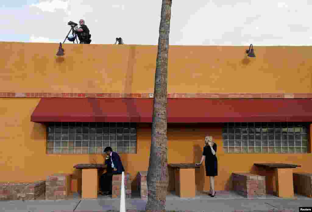 U.S. President Joe Biden&rsquo;s director of speech writing Vinay Reddy works at his laptop and White House economic advisor Lael Brainard talks on her phone as members of the Secret Service keep watch atop a Mexican restaurant where Biden was holding a campaign event in Phoenix, Arizona, March 19, 2024.