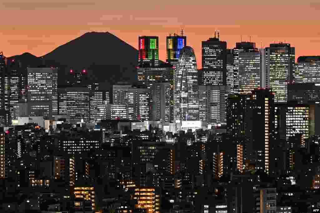 Mount Fuji (back L), Japan&#39;s highest mountain at 3,776 meters (12,389 feet), is silhouetted during sunset behind the high-rise buildings of the Shinjuku area in downtown Tokyo.