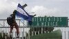 Un migrante hondureño sostiene su bandera y sube a la valla en Ciudad Hidalgo, México. Octubre 18, 2018.
