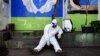 A health agency official, seen alongside his disinfectant dispenser, rests by the entrance to a public toilet as other colleagues (not pictured) conduct polymerase chain reaction (PCR) testing for the COVID-19 coronavirus at a bus station in Bandung, West
