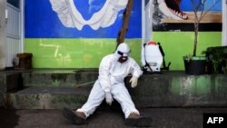 A health agency official, seen alongside his disinfectant dispenser, rests by the entrance to a public toilet as other colleagues (not pictured) conduct polymerase chain reaction (PCR) testing for the COVID-19 coronavirus at a bus station in Bandung, West