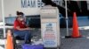 A poll worker wears personal protective equipment as she monitors a ballot drop box for mail-in ballots outside of a polling station during early voting, in Miami Beach, Florida. Aug. 7, 2020.